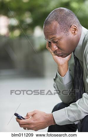 Stock Photo - Black businessman text messaging on cell phone. Fotosearch