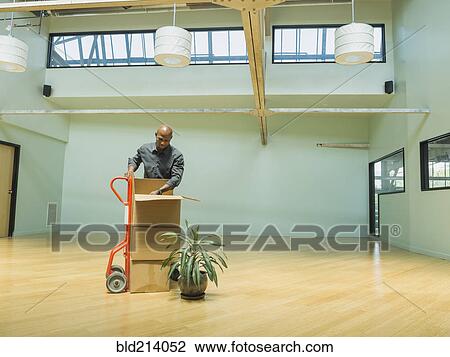 Stock Image - Black businessman unpacking cardboard boxes in empty office. Fotosearch