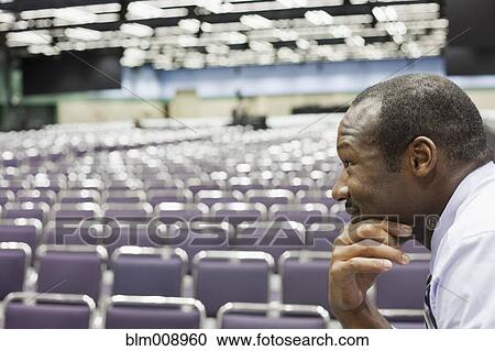 Stock Image - Black businessman waiting in empty conference center. Fotosearch
