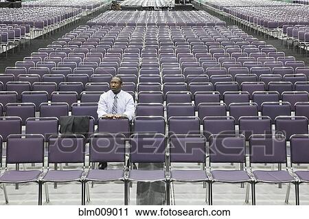 Stock Image - Black businessman waiting in empty conference center. Fotosearch