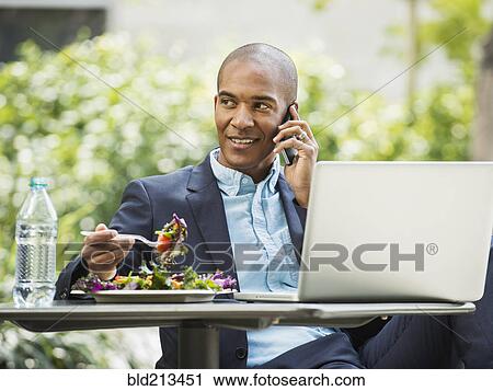 Stock Image - Black businessman working and eating lunch outdoors. Fotosearch