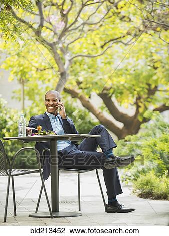 Stock Image - Black businessman working and eating lunch outdoors. Fotosearch