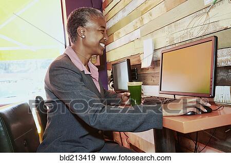 Stock Photo - Black businesswoman drinking juice at internet cafe. Fotosearch