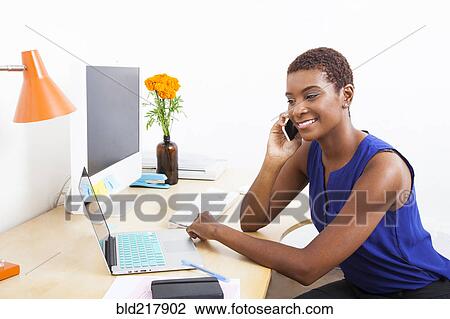 Black businesswoman talking on cell phone at office desk View Large Photo Image Stock Image - Black businesswoman talking on cell phone at office desk. Fotosearch