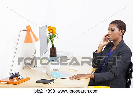 Stock Photo - Black businesswoman talking on cell phone at office desk. Fotosearch