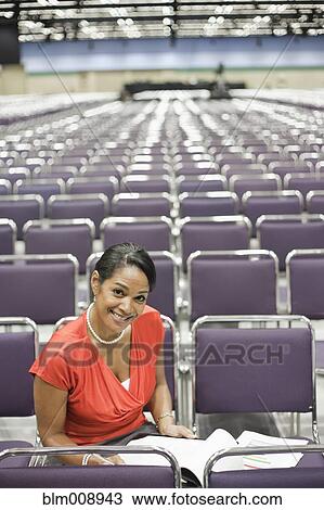 Stock Image - Black businesswoman waiting in empty conference center. Fotosearch