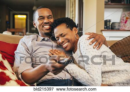 Stock Photo - Black couple watching television on sofa. Fotosearch