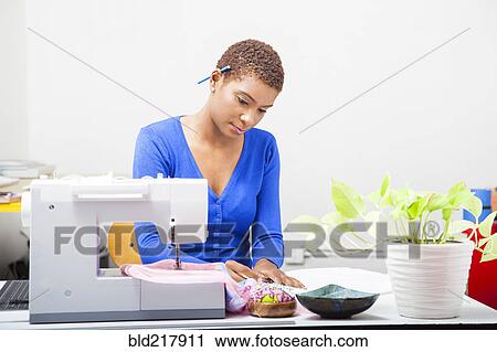 Stock Image - Black dressmaker using sewing machine. Fotosearch