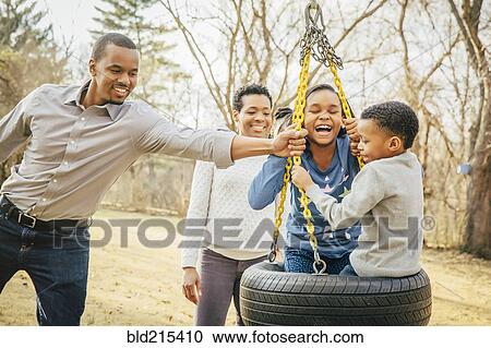 Stock Image - Black family playing on tire swing. Fotosearch