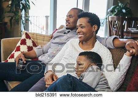 Stock Image - Black family watching television on sofa. Fotosearch