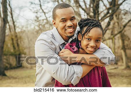 Stock Photograph - Black father and daughter hugging outdoors. Fotosearch
