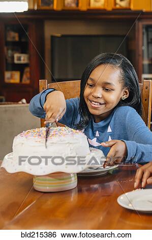 Stock Photograph - Black girl cutting cake at birthday party. Fotosearch