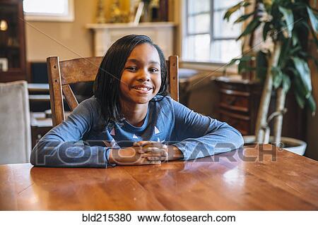 Stock Image - Black girl smiling at table. Fotosearch