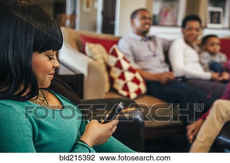 Stock Image - Black girl using cell phone in living room. Fotosearch