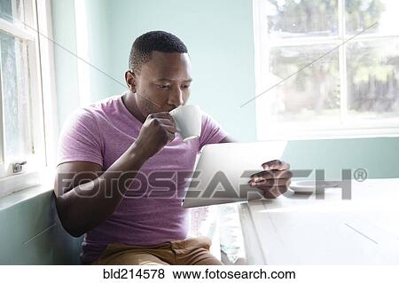 Black man drinking coffee and using digital tablet View Large Photo Image Stock Photo - Black man drinking coffee and using digital tablet. Fotosearch