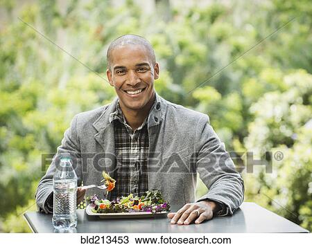 Stock Image - Black man eating lunch in urban park. Fotosearch