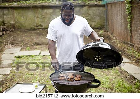 Stock Image - Black man grilling hamburgers at backyard barbecue. Fotosearch