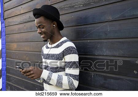 Stock Photo - Black man listening to mp3 player near wooden wall. Fotosearch
