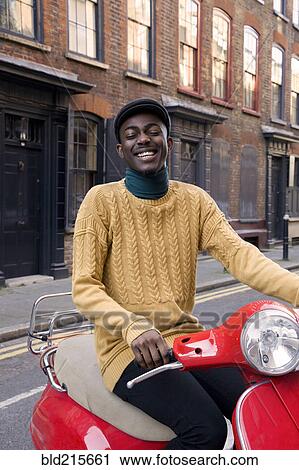 Stock Image - Black man riding scooter on urban street. Fotosearch