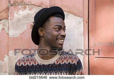 Stock Photograph - Black man sitting by dilapidated building. Fotosearch