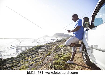Black man texting cell phone near car at coast View Large Photo Image Stock Image - Black man texting cell phone near car at coast. Fotosearch