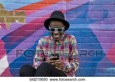 Stock Image - Black man using cell phone near colorful wall. Fotosearch