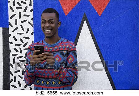 Stock Photography - Black man using cell phone near colorful wall. Fotosearch