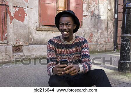 Picture - Black man using cell phone on urban sidewalk. Fotosearch