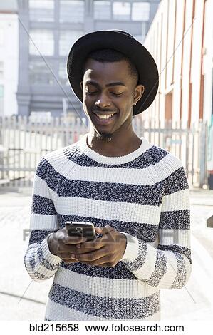 Stock Photo - Black man using cell phone on urban sidewalk. Fotosearch
