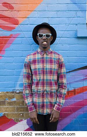 Stock Image - Black man wearing sunglasses near colorful wall. Fotosearch