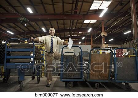 Stock Photo - Black manager standing with hand carts in factory. Fotosearch