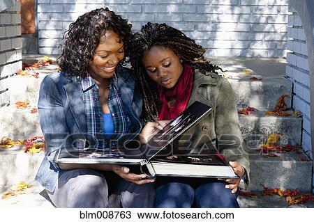 Black mother and daughter sitting on front stoop looking at photo album View Large Photo Image Stock Image - Black mother and daughter sitting on front stoop looking at photo album. Fotosearch