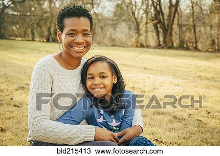 Stock Image - Black mother and daughter sitting outdoors. Fotosearch