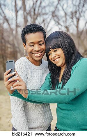 Stock Image - Black mother and daughter taking selfie outdoors. Fotosearch