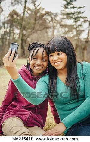 Stock Photo - Black sisters taking selfie outdoors. Fotosearch