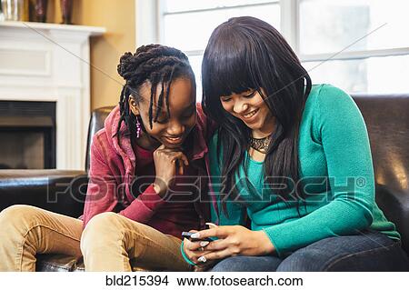 Black sisters using cell phone on sofa View Large Photo Image Picture - Black sisters using cell phone on sofa. Fotosearch