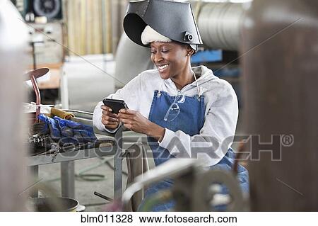 Stock Photo - Black welder text messaging on cell phone on factory. Fotosearch