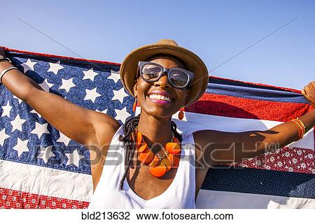 Stock Image - Black woman holding American flag under blue sky. Fotosearch
