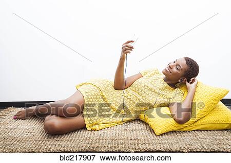 Stock Photo - Black woman listening to mp3 player on carpet. Fotosearch
