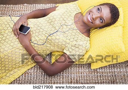 Stock Photo - Black woman listening to mp3 player on carpet. Fotosearch