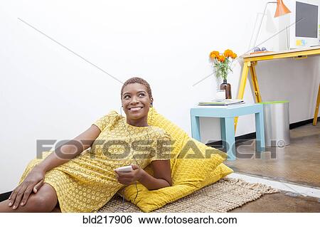 Stock Photograph - Black woman listening to mp3 player on floor. Fotosearch
