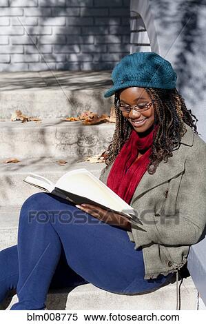Stock Photography - Black woman reading book on front stoop. Fotosearch