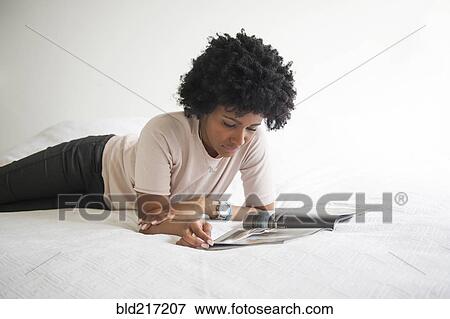 Stock Photo - Black woman reading magazine on bed. Fotosearch