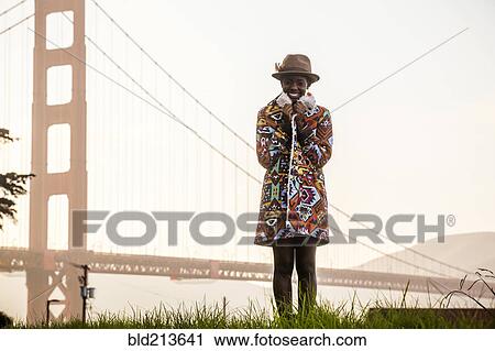 Stock Image - Black woman wearing colorful coat by Golden Gate Bridge, San Francisco, California, United States. Fotosearch