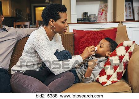 Stock Photo - Black woman wiping nose of son on sofa. Fotosearch