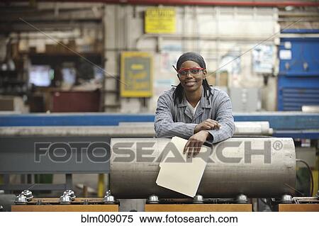 Stock Photography - Black worker leaning on metal pipe in factory. Fotosearch