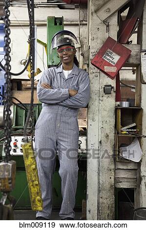 Stock Photo - Black worker leaning on post in factory. Fotosearch