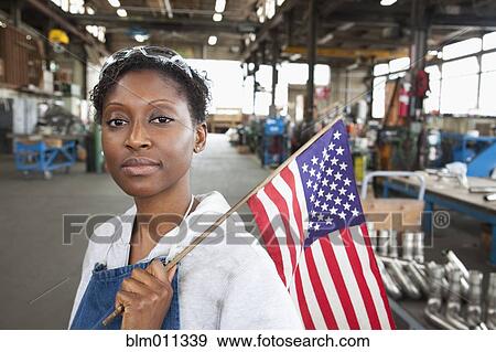 Stock Photo - Black worker standing in factory with American flag. Fotosearch