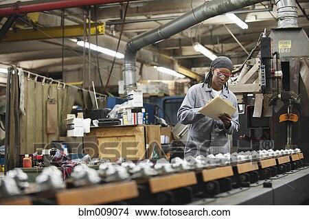 Picture - Black worker viewing equipment in factory. Fotosearch