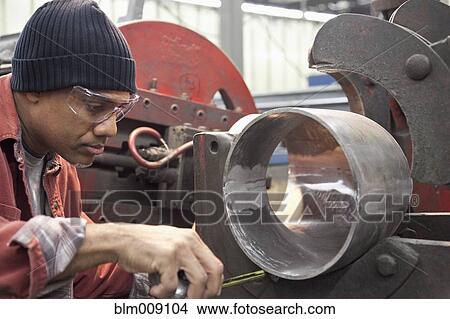 Picture - Black worker working in metal pipe in factory. Fotosearch